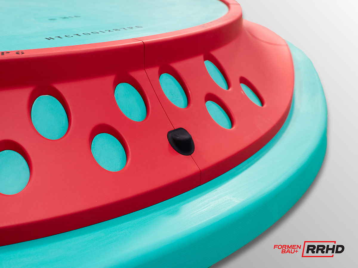 Detailansicht eines mehrfarbigen Gießereimodells mit einer roten, gelochten Wandstruktur und einer türkisfarbenen Basis und Deckfläche. Die runde Form des Modells lässt auf eine rotierende Maschinenkomponente oder ein Gehäuseteil schließen. Eine Trennfuge und ein schwarzes Passstück sind sichtbar