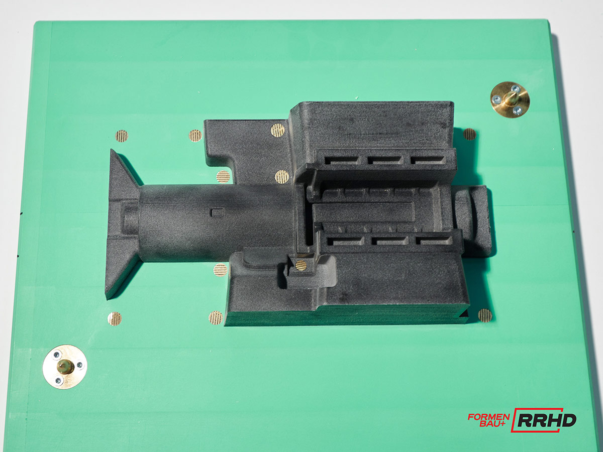 Schwarzes Gießereimodell eines komplexen technischen Bauteils. Es handelt sich um eine Seite des Kernkastens. Zu sehen sind die metallischen Scheibendübel zur Führung.