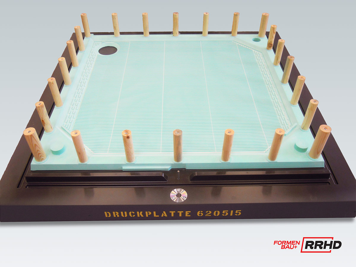 Gießereimodell einer Druckplatte, montiert auf einer schwarzen Formplatte. Die Modellfläche ist türkisfarben mit einem regelmäßigen Rastermuster versehen. Rundherum sind zahlreiche senkrechte Holzspeiser.